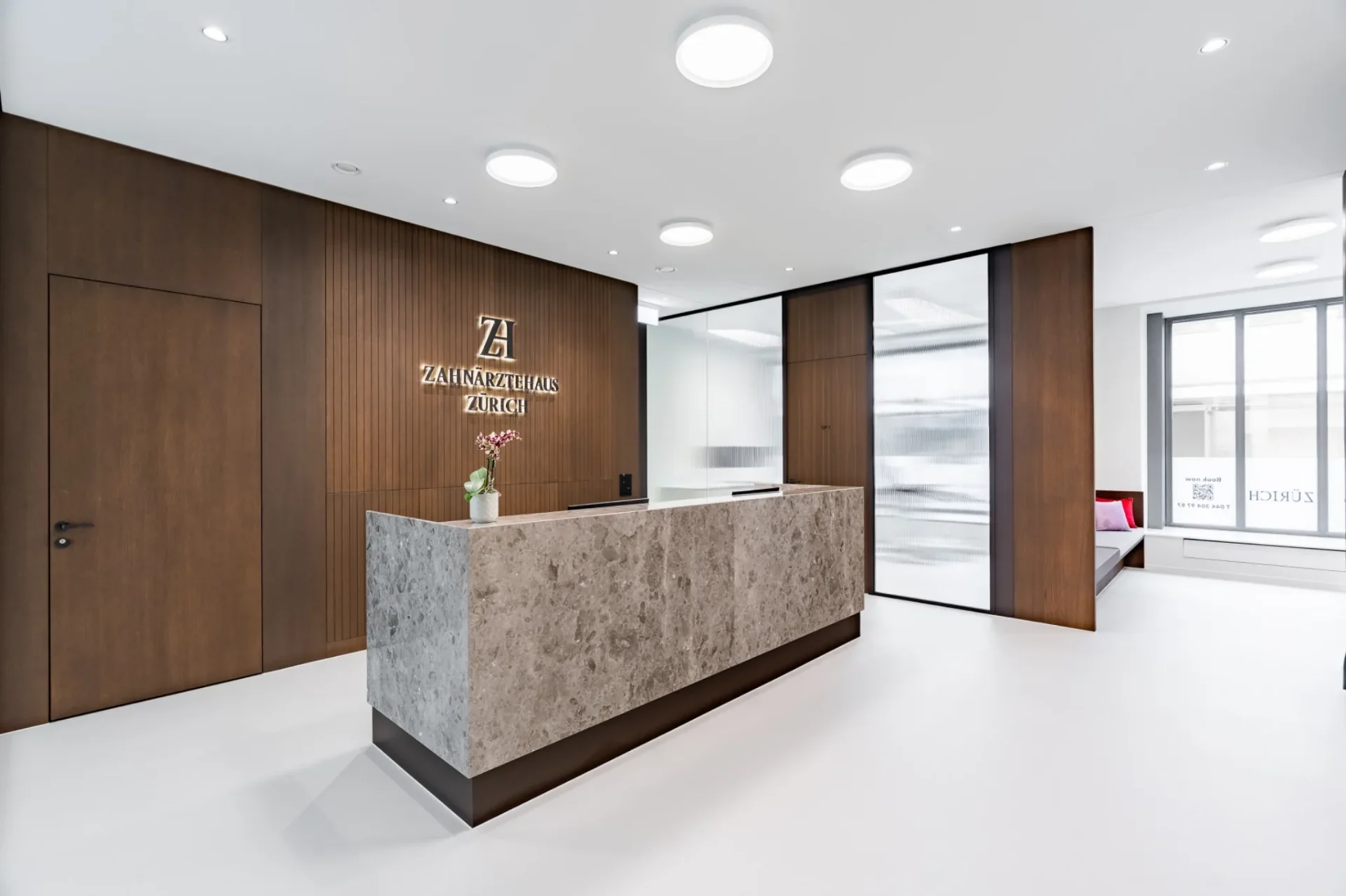 Empfangsbereich im Zahnärztehaus Zürich mit Steintheke und Logo an der Holzwand