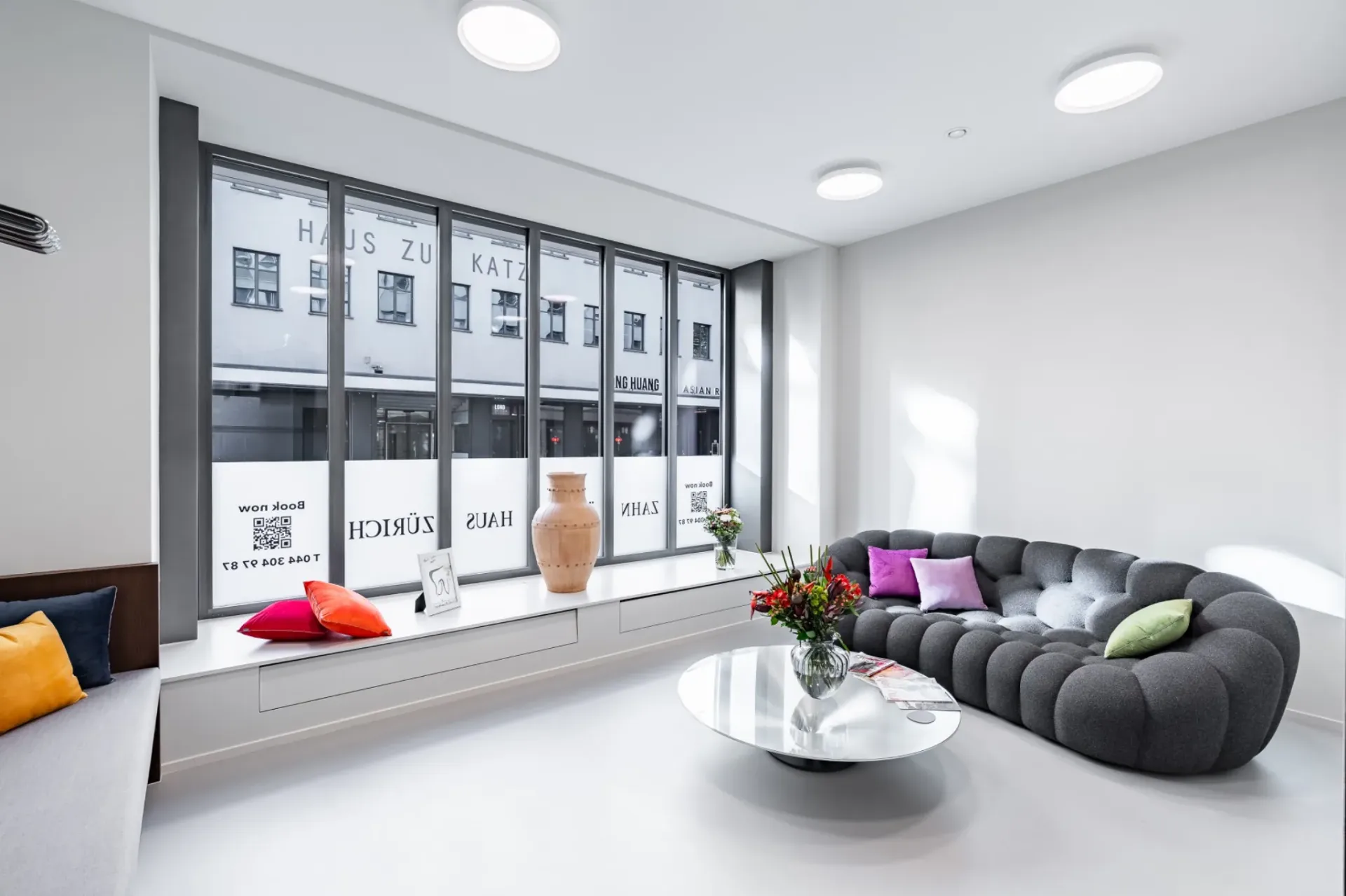 Wartebereich im Zahnärztehaus Zürich mit Sofa, Couchtisch und großen Fenstern